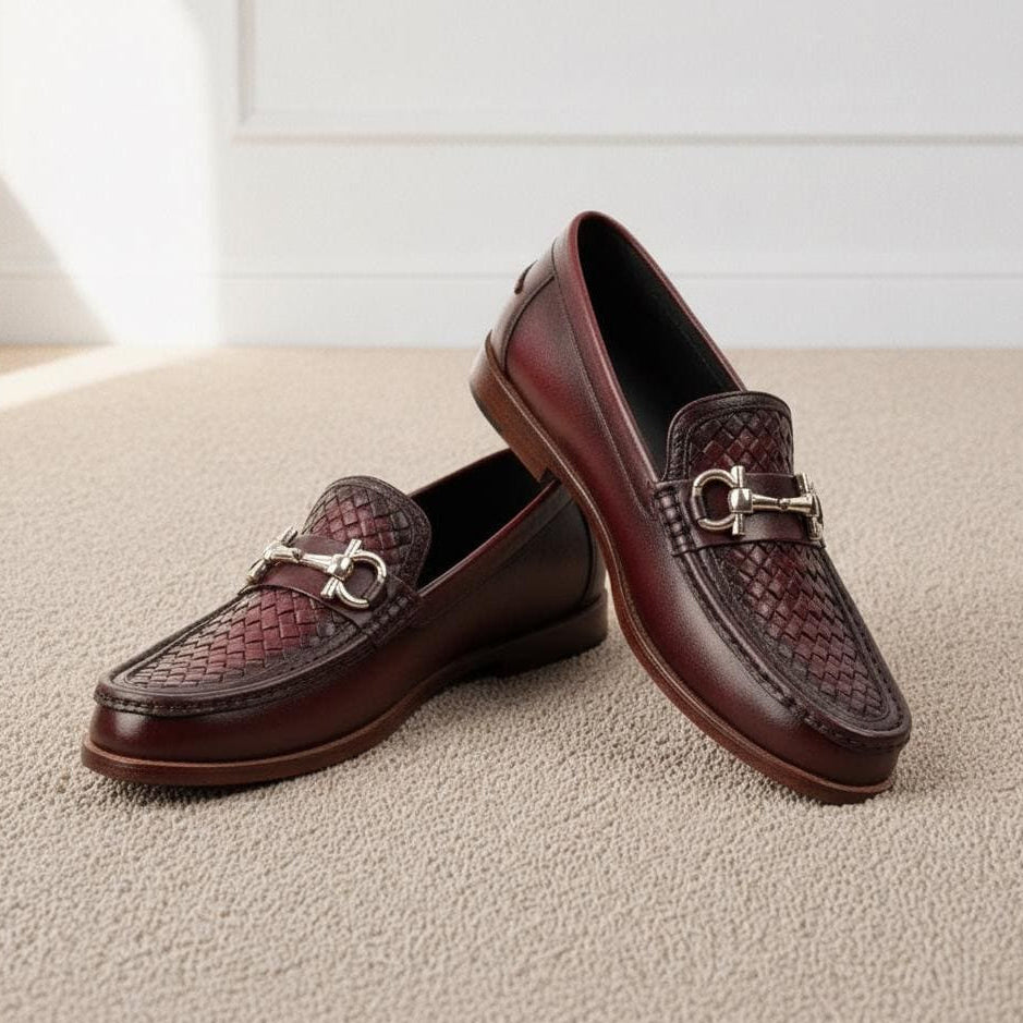 A pair of dark brown leather loafers with a woven pattern on the toe and a silver-tone horsebit detail, displayed on a beige carpeted floor.